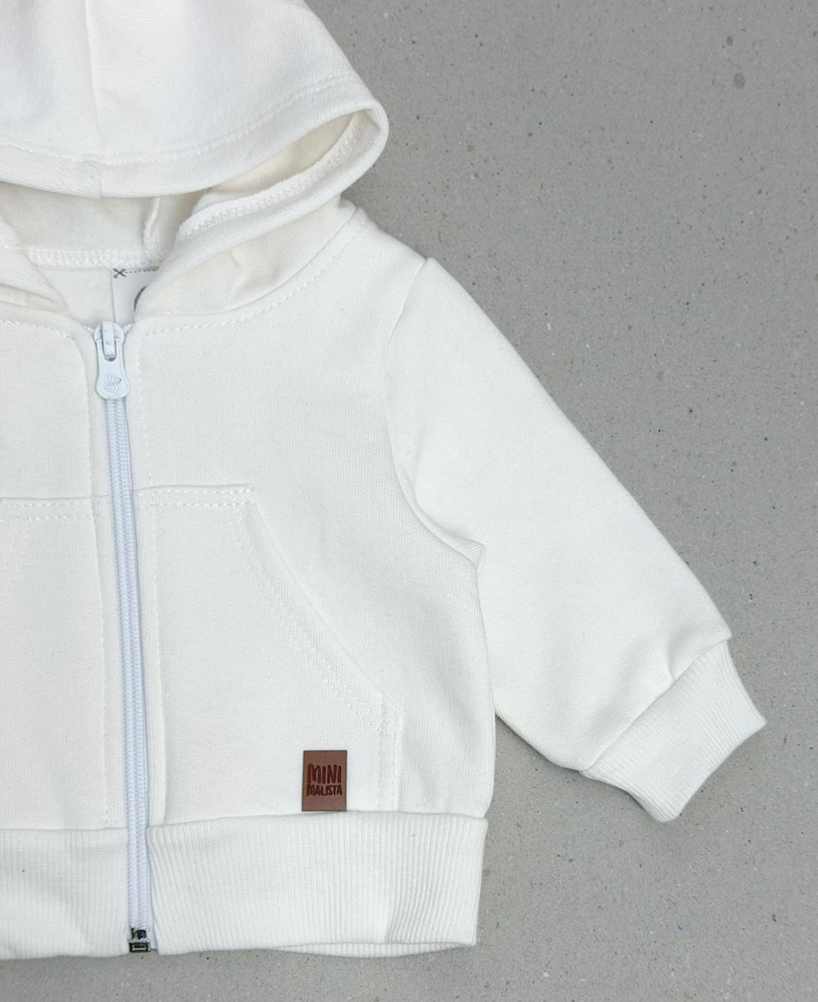 Casaco Off-White Infantil Peluciado MiniMalista Baby — criança usando o casaco em ambiente escandinavo minimalista, mostrando a modelagem generosa e o capuz confortavelmente amplo. Marca criada por mãe pra crianças com pele sensível.