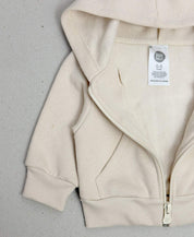 Casaco Infantil Bege Claro Peluciado MiniMalista Baby — vista lateral mostrando o corte folgado proposital, feito pra usar como terceira camada sobre body ou camiseta canelada. Cobre-zíper interno protege o queixo. Unissex, do bebê aos 5-6 anos.