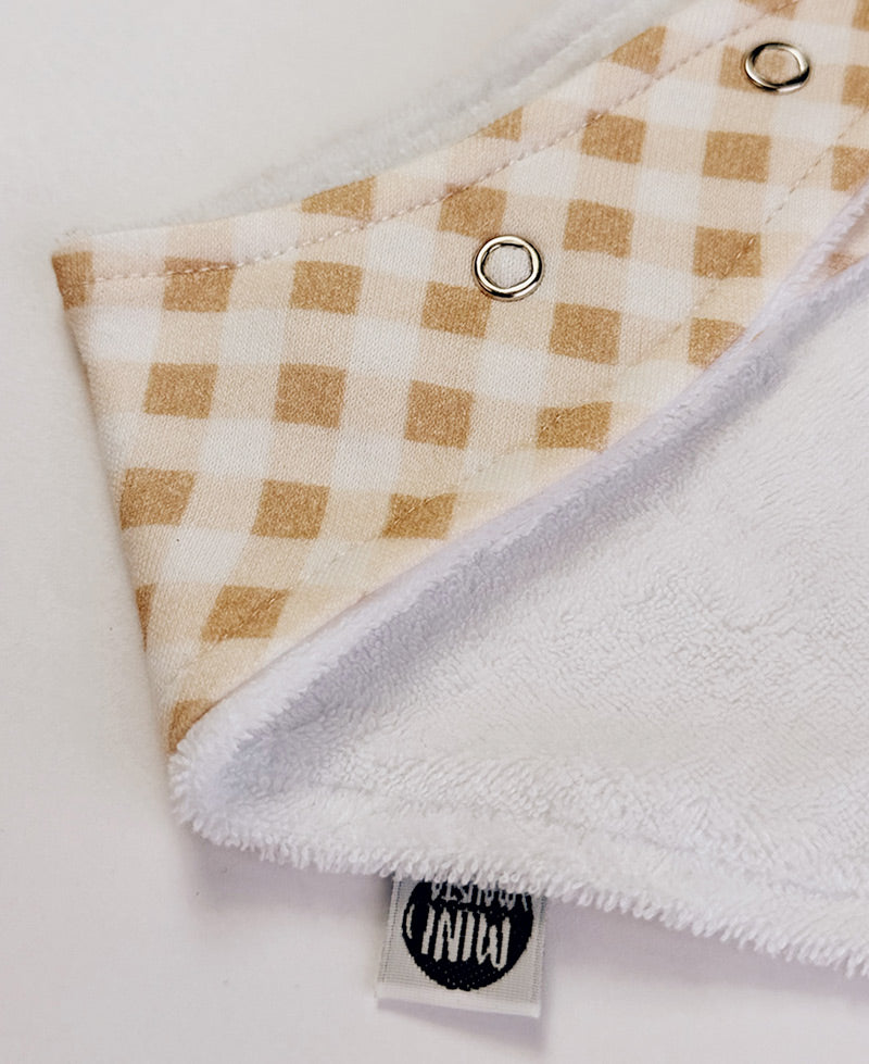 Detalhe do xadrez vichy bege e da malha de algodão do Babador Bandana MiniMalista. Babador de bebê unissex, estampa atóxica, acabamento macio.