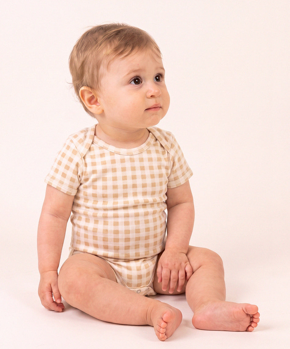 Bebê vestindo o Body Manga Curta Vichy Bege MiniMalista, vista frontal. Body de bebê em algodão com gola americana, xadrez vichy bege, unissex menino e menina.