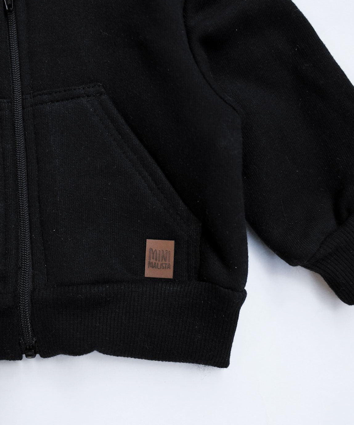 MiniMalista Casaco Moletom Capuz e Zíper Peluciado em Preto, vista frontal com capuz e bolsos. 100% algodão peluciado quentinho, casaco infantil unissex coringa absoluto pra qualquer dia frio.