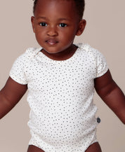 Bebê sorrindo vestindo o Body Manga Curta Bolinhas Claro MiniMalista. Body de bebê em algodão com poá delicado, unissex.